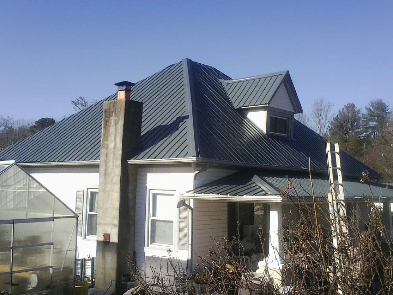 Dark blue standing seam metal roof on a white farmhouse with dormer — Slate & Tile Roof Repair by Roofing Brothers in Heiskell