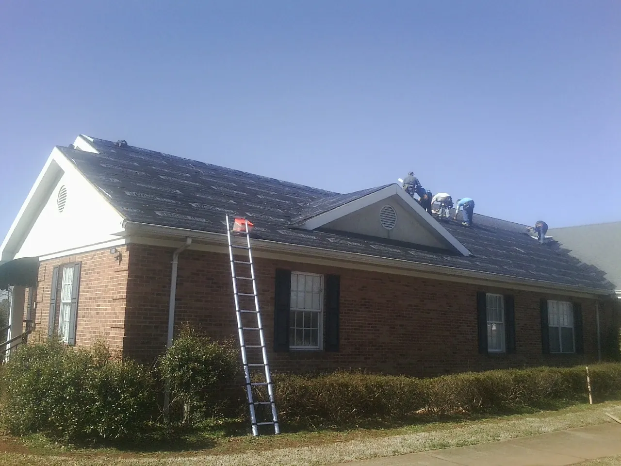 Crew tearing shingles off a brick ranch roof with a ladder set — Metal Roof Repair work by our crew in Heiskell