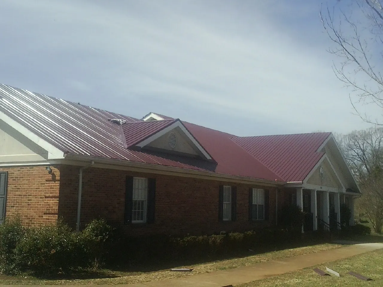 Red metal roof with gabled entries on a long brick building, from a Hail Damage Roof Repair job in Heiskell