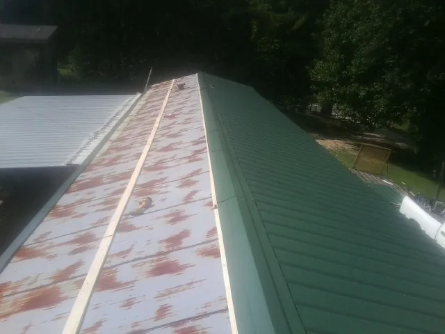 Old rusted panels beside newly installed green metal roofing — Wind Damage Roof Repair by Roofing Brothers in Heiskell