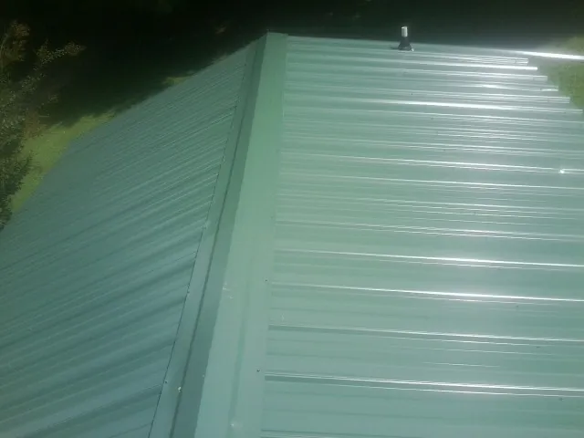 New green metal panels meeting at the ridge of a roof — Flat Roof Repair work by our crew in Heiskell