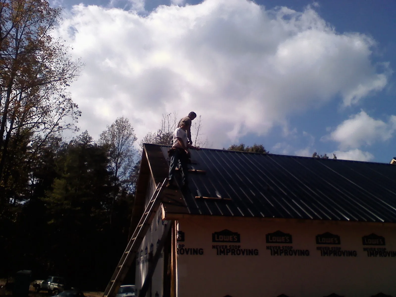 Roofer fastening dark metal panels high against a cloudy sky, from a Roof Inspection job in Heiskell