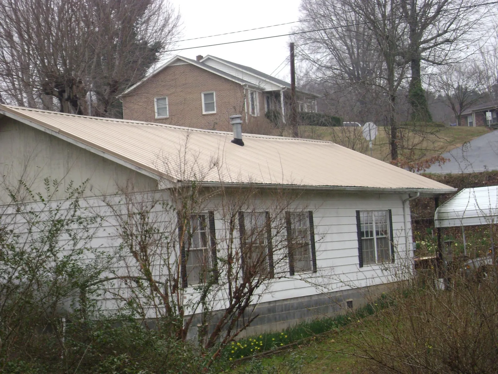 Tan metal roof on a white sided house set into a hillside — Commercial Roofing by Roofing Brothers in Heiskell