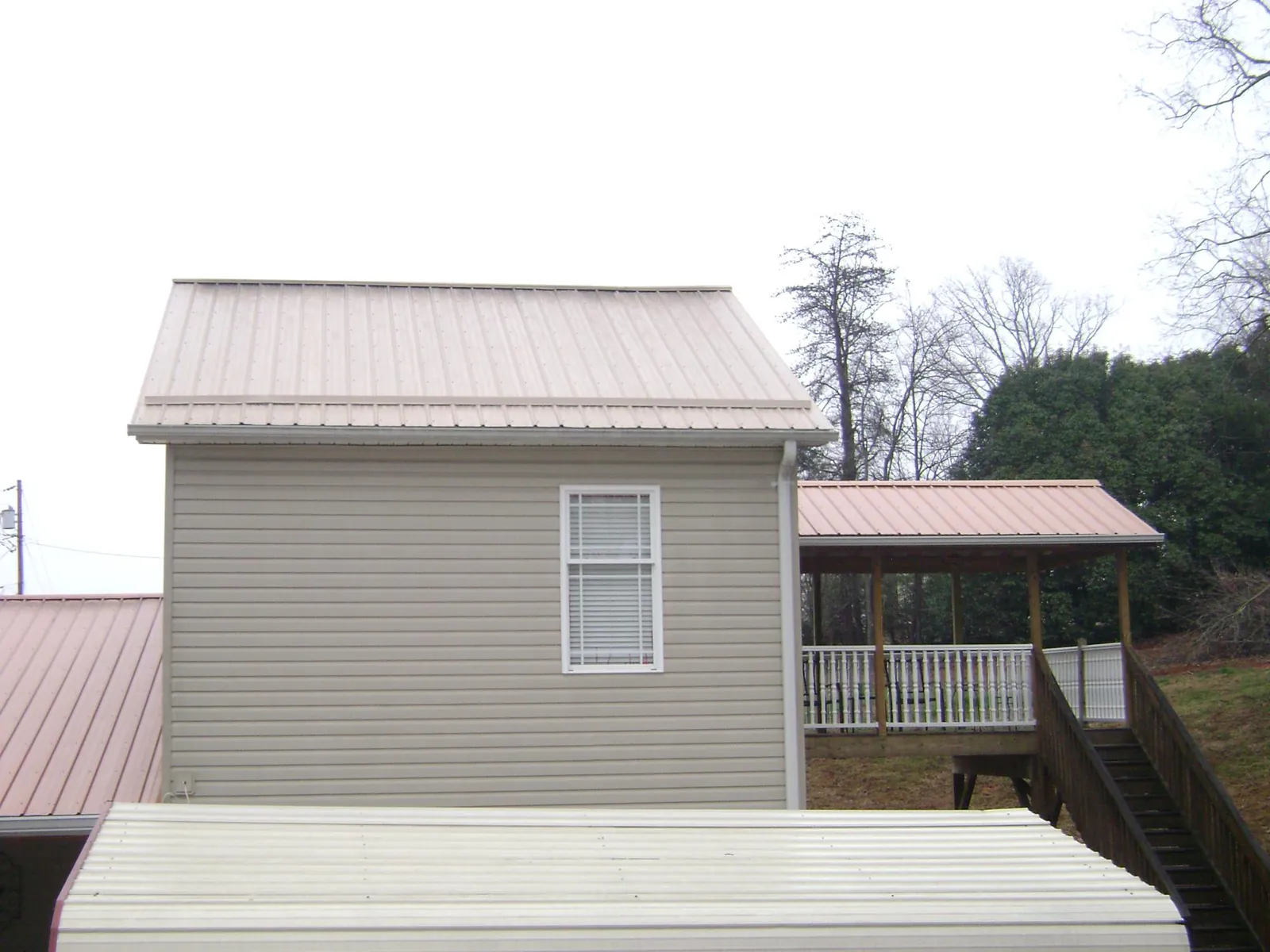 Tan metal roofs on a two story addition and attached porch, from a Roof Replacement job in Heiskell